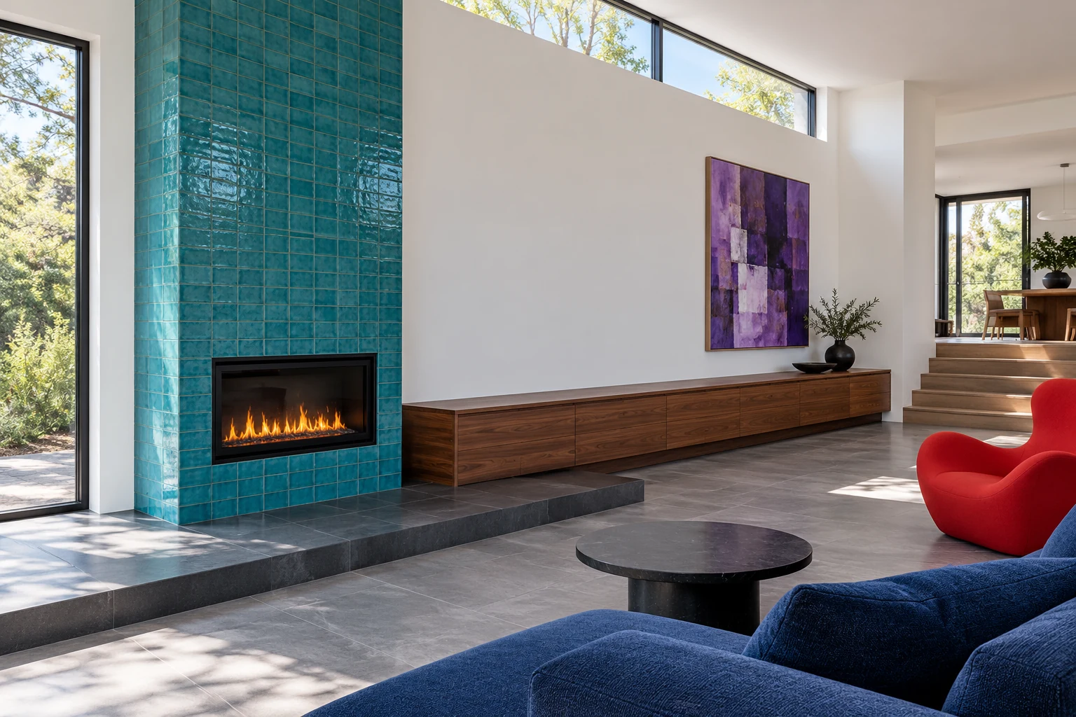 Asymmetric turquoise fireplace beside low walnut storage and a red chair