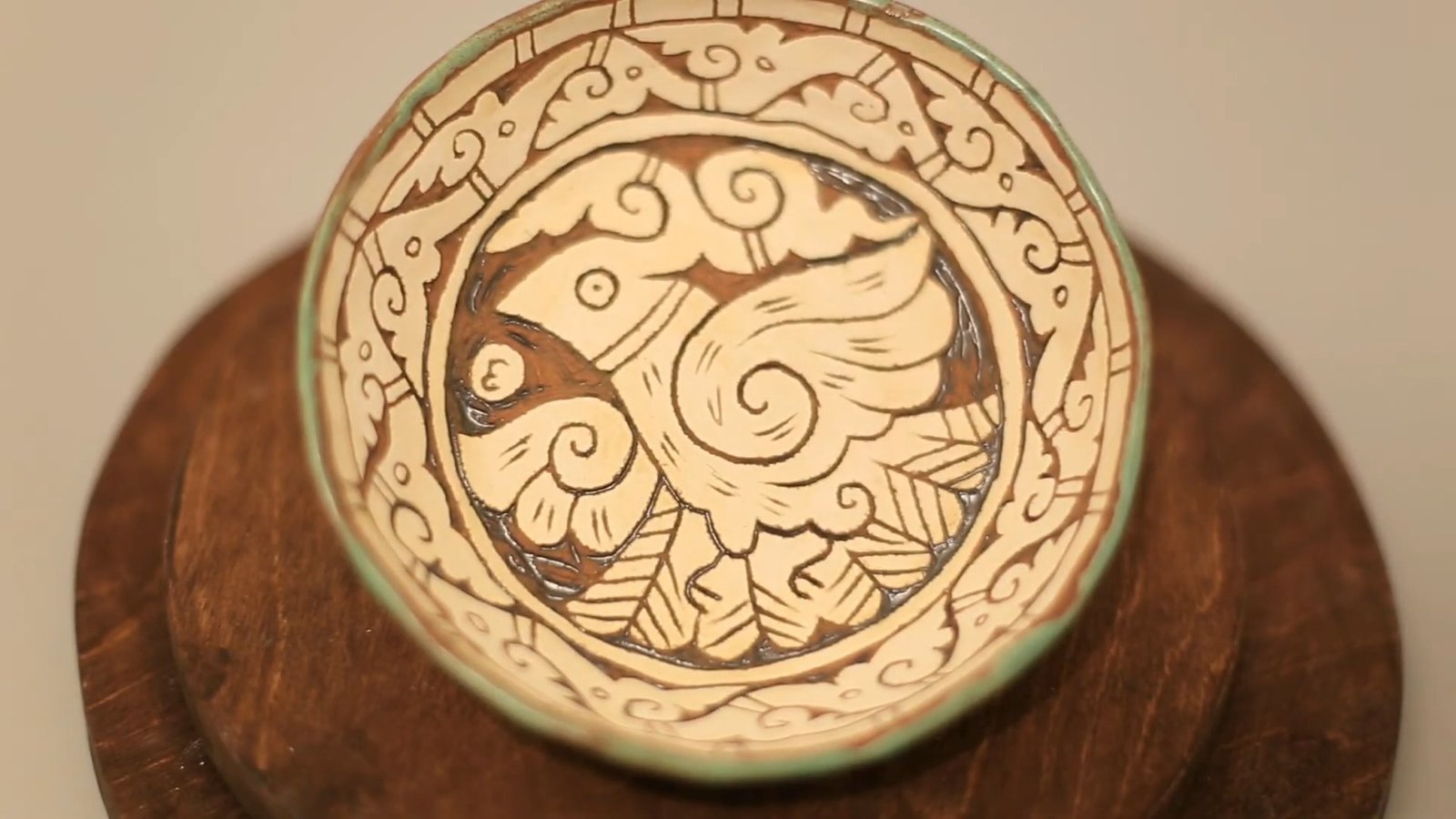 Finished sgraffito plate with a cream bird motif, brown carved outlines, a patterned border and a green rim.