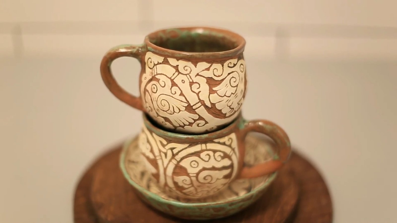 Two finished handmade mugs with cream and brown carved bird motifs and green accents along their rims.