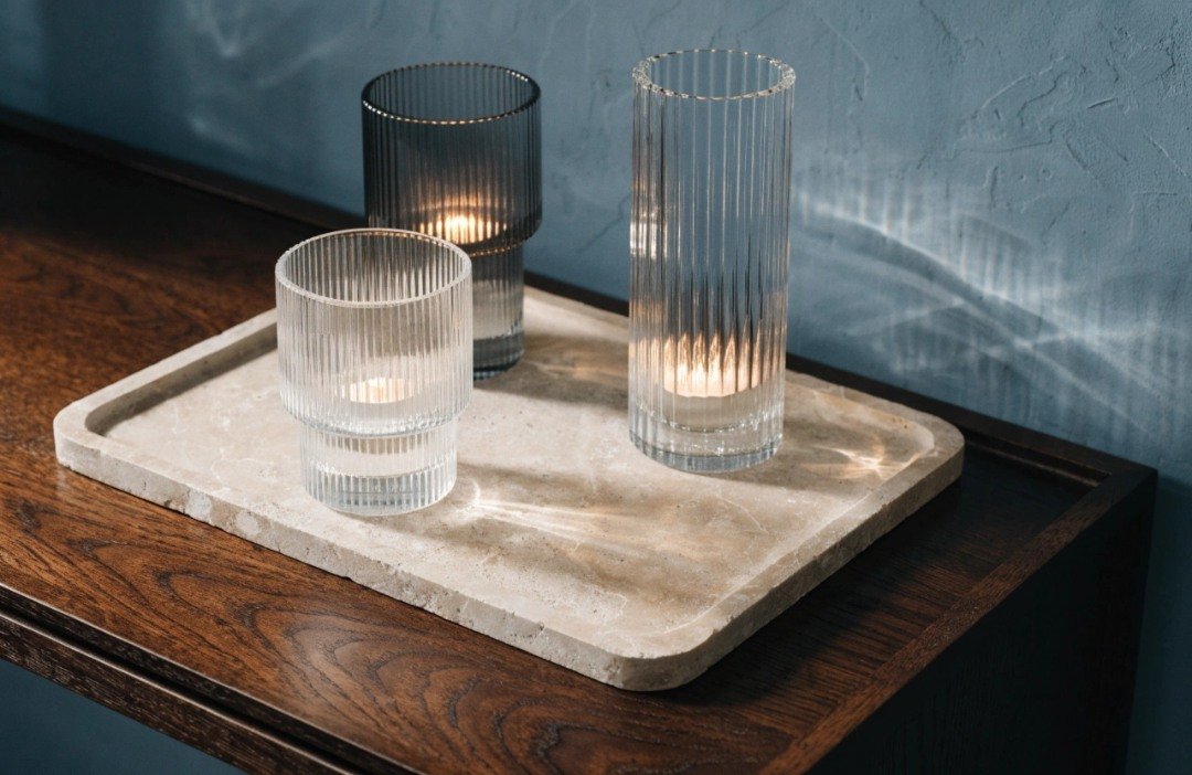 Three ribbed-glass votive holders in clear and smoky gray glass arranged at different heights on a limestone tray with LED tealights.