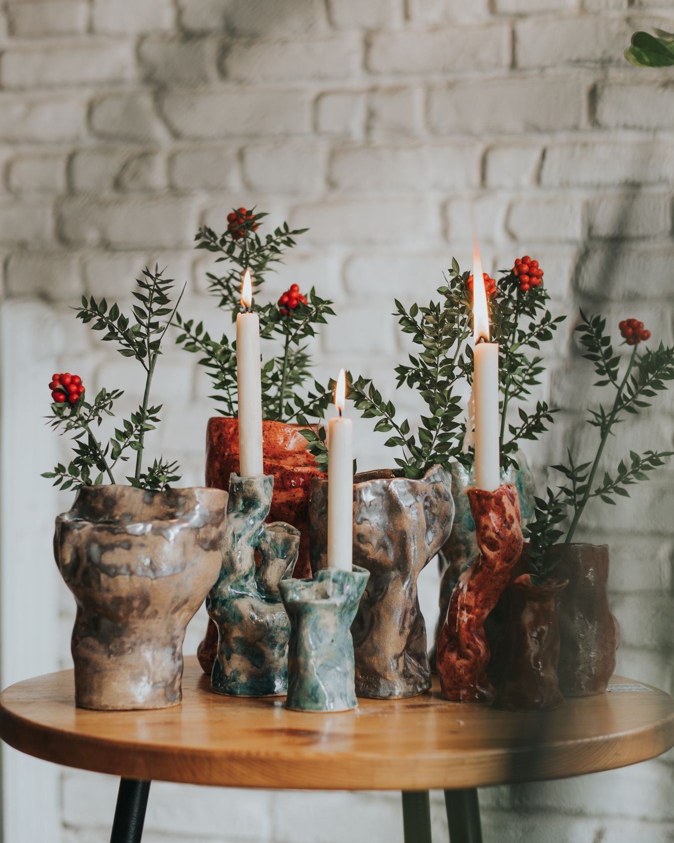 Earthy textured ceramic candle holders styled beside greenery on a warm wood table