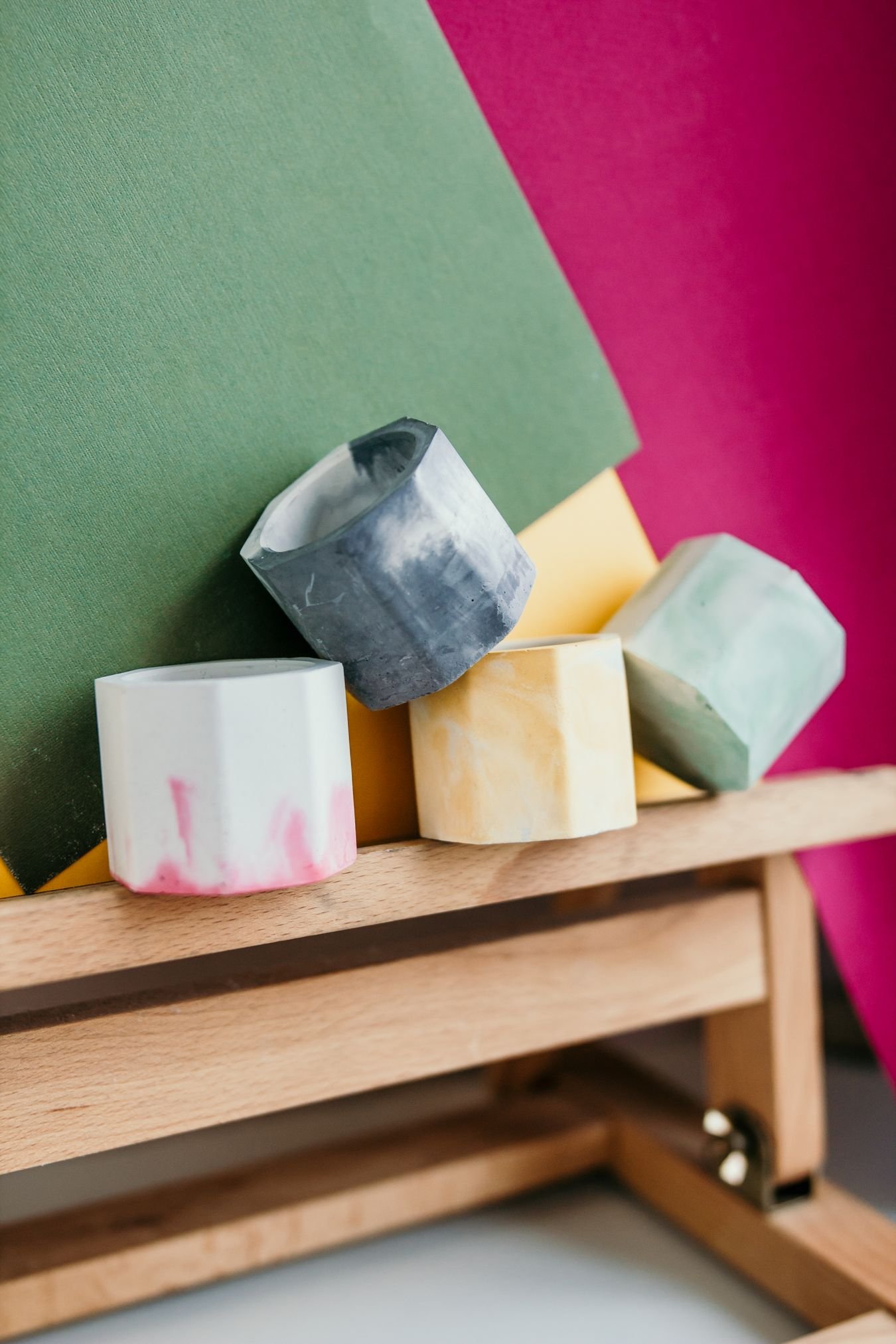 Vibrant geometric colorful handmade candle holders on a wood shelf against a patterned wall