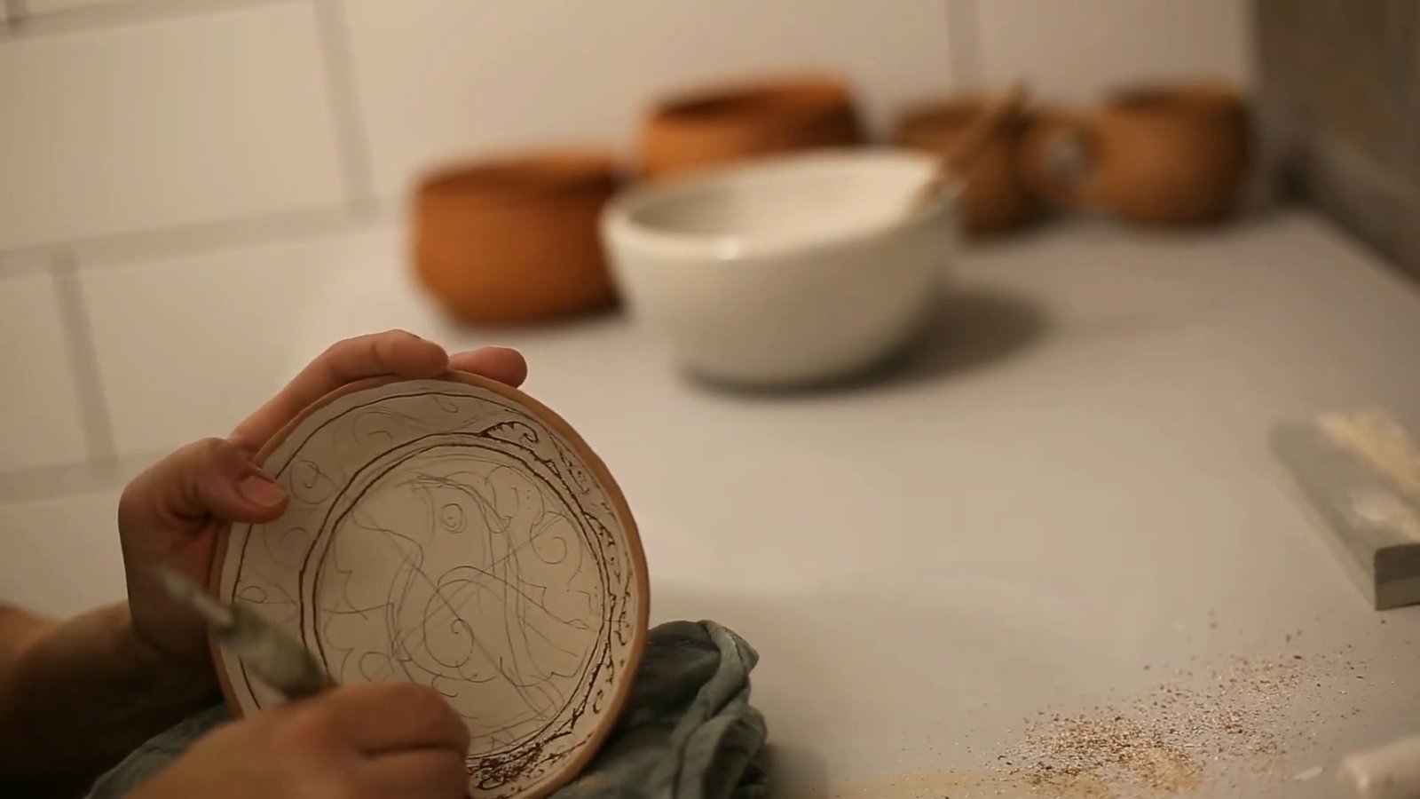 Circular design lightly outlined across the pale surface of a small clay plate held upright.