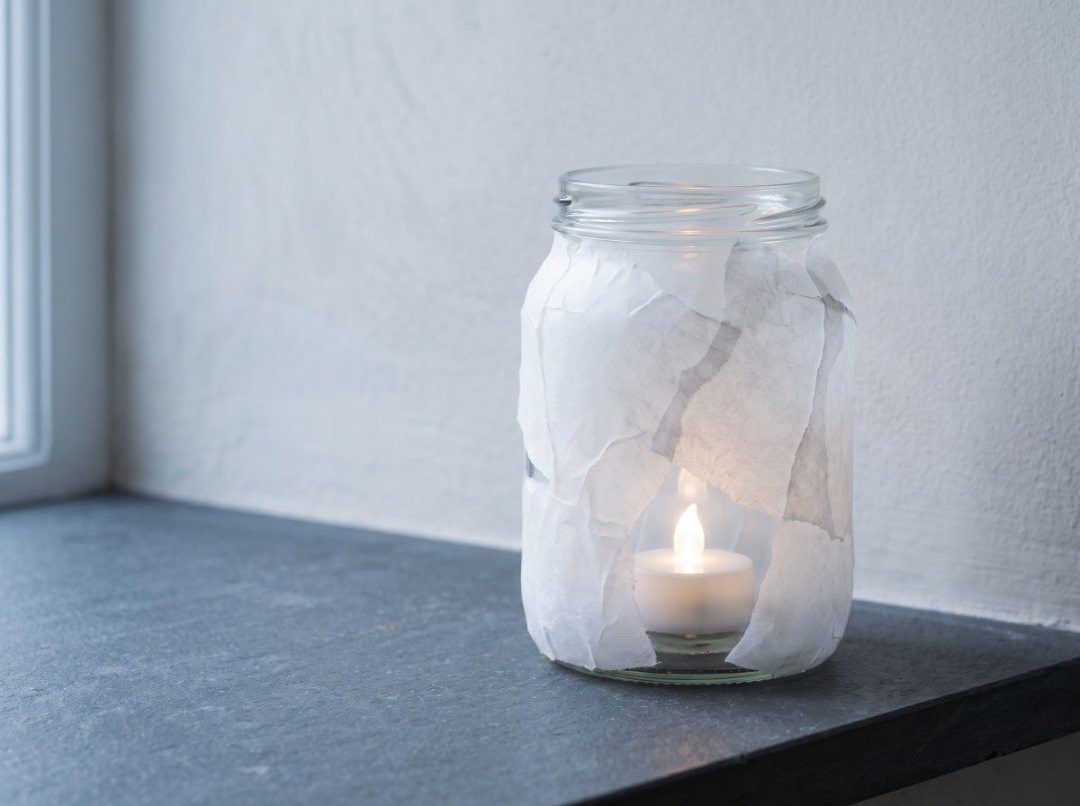 DIY frosted-tissue glass jar lantern with overlapping white paper layers and a warm battery-operated LED tealight inside.