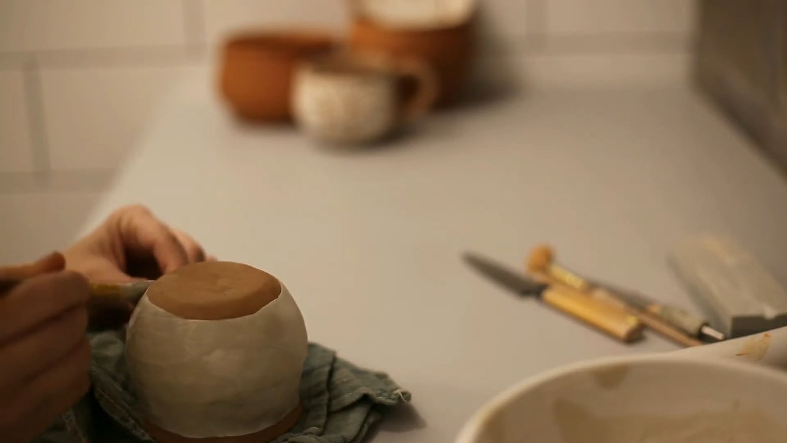 Brown clay mug with a pale surface coating, resting upside down beside brushes in a pottery workspace.